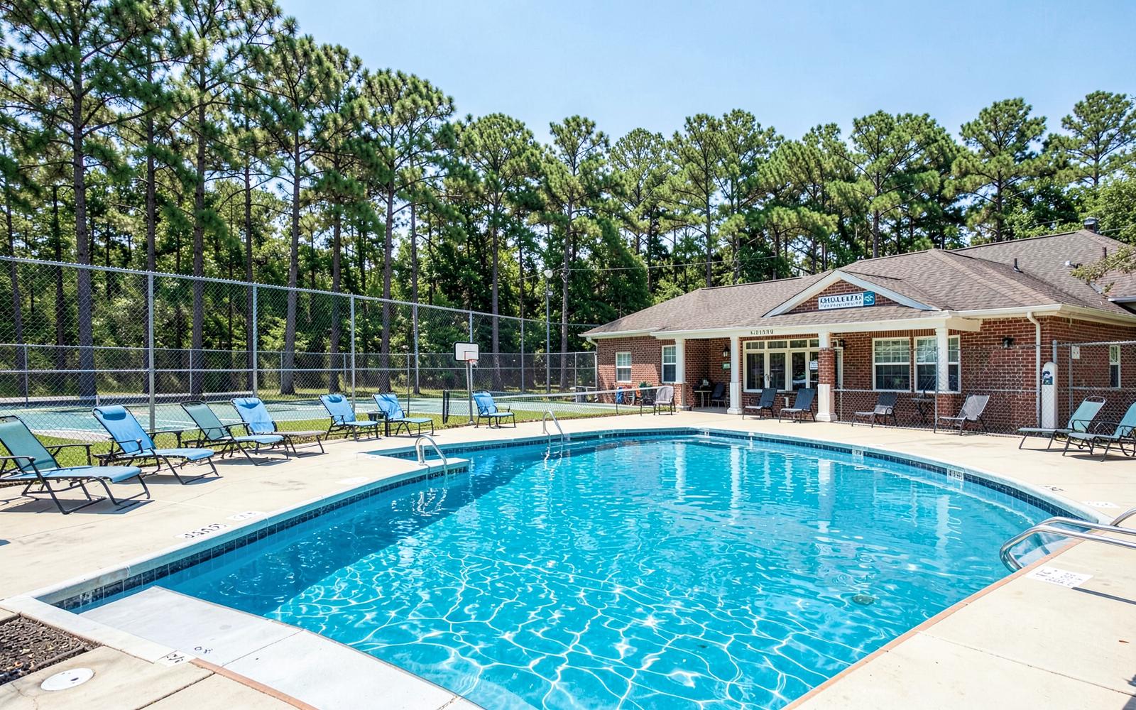 Blue pool water, lounge chairs, and tennis courts behind pines at a south Charlotte neighborhood swim and tennis club