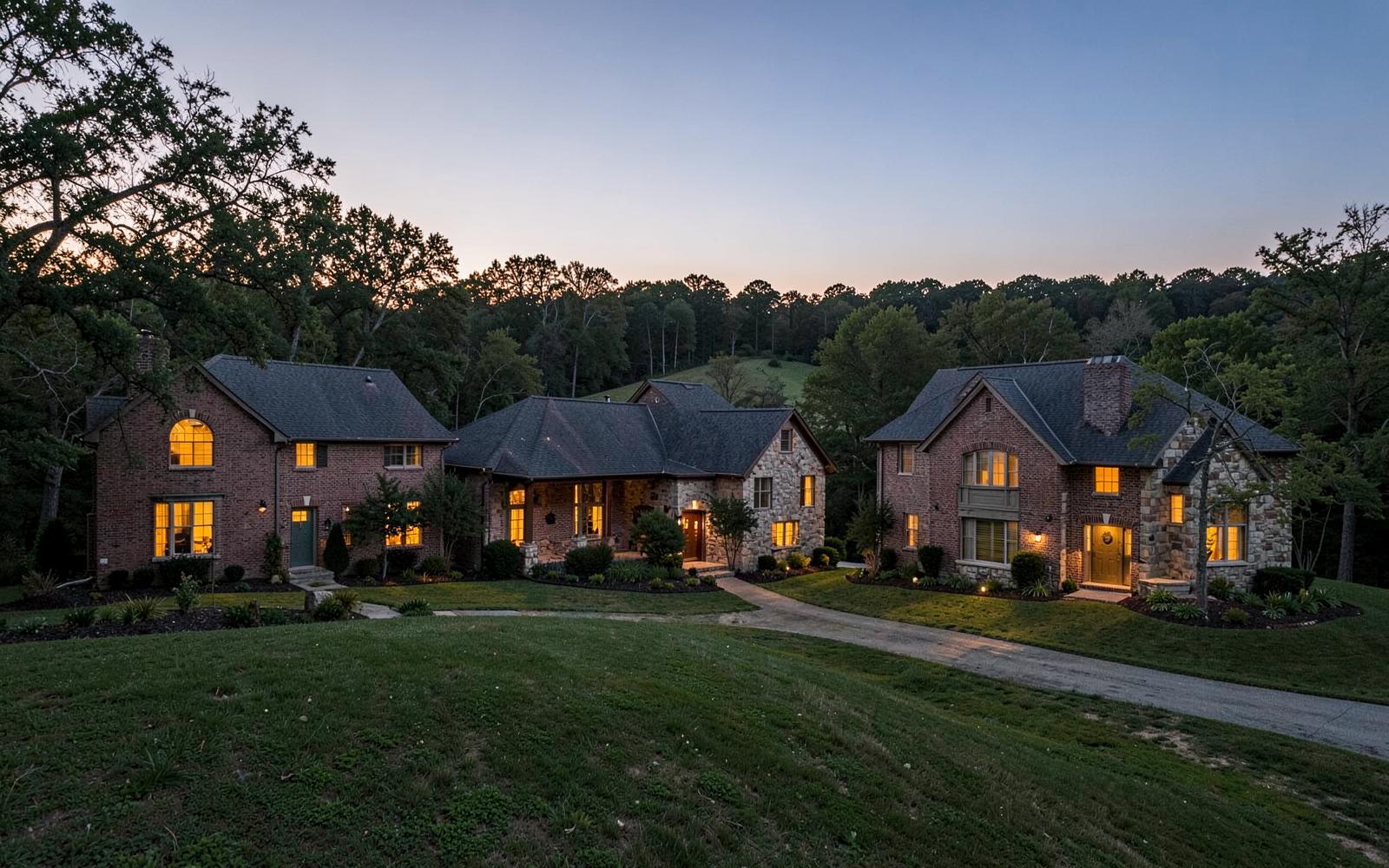 Dusk light and warm windows on large brick and stone traditional homes across rolling wooded lots in south Charlotte