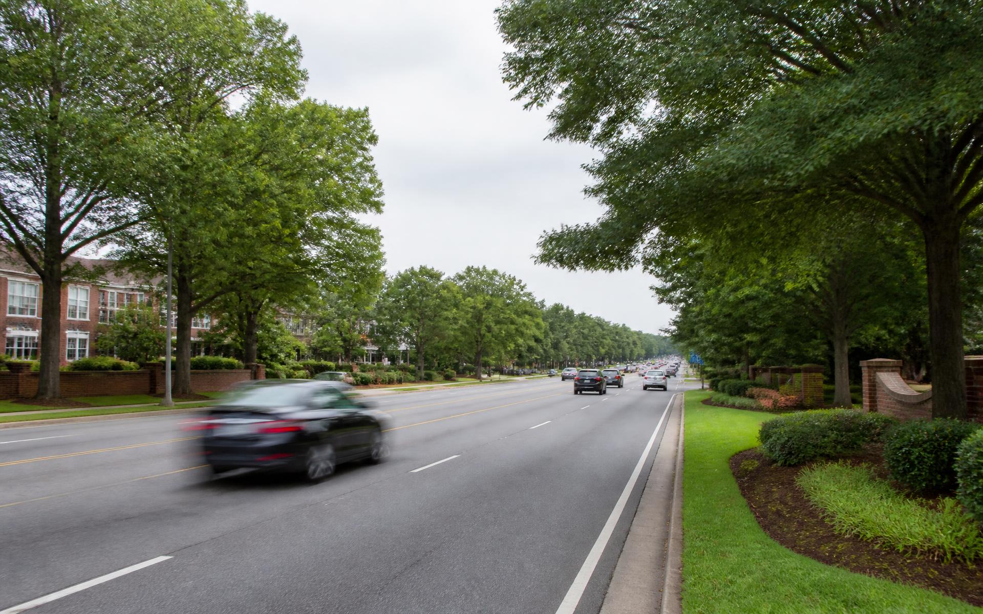 A tree-lined four-lane arterial road with brick entry walls in south Charlotte, North Carolina